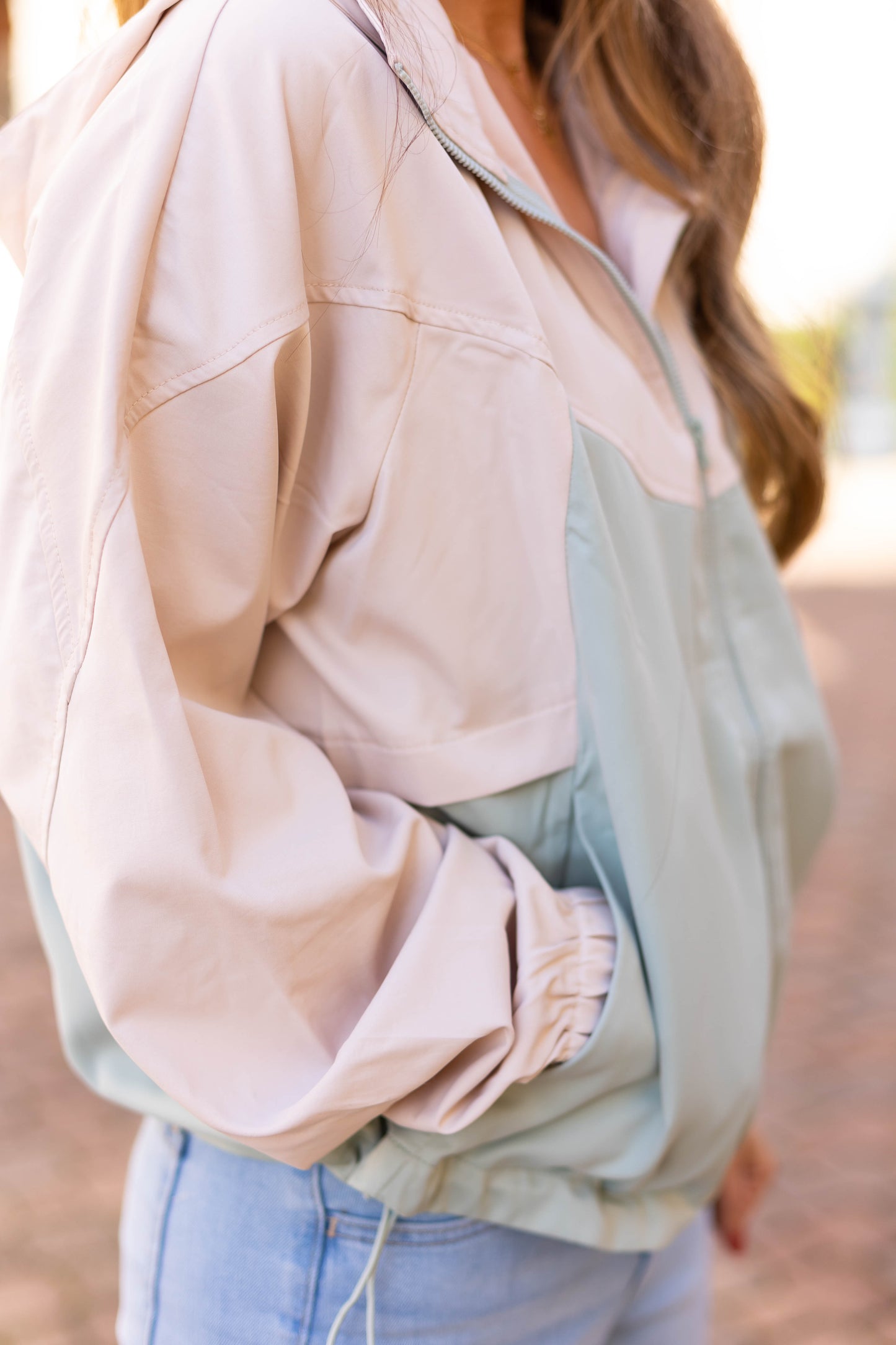 A person outdoors, hands in pockets, wears a Callie Active Jacket by Dogwood Cloth in a pastel color.