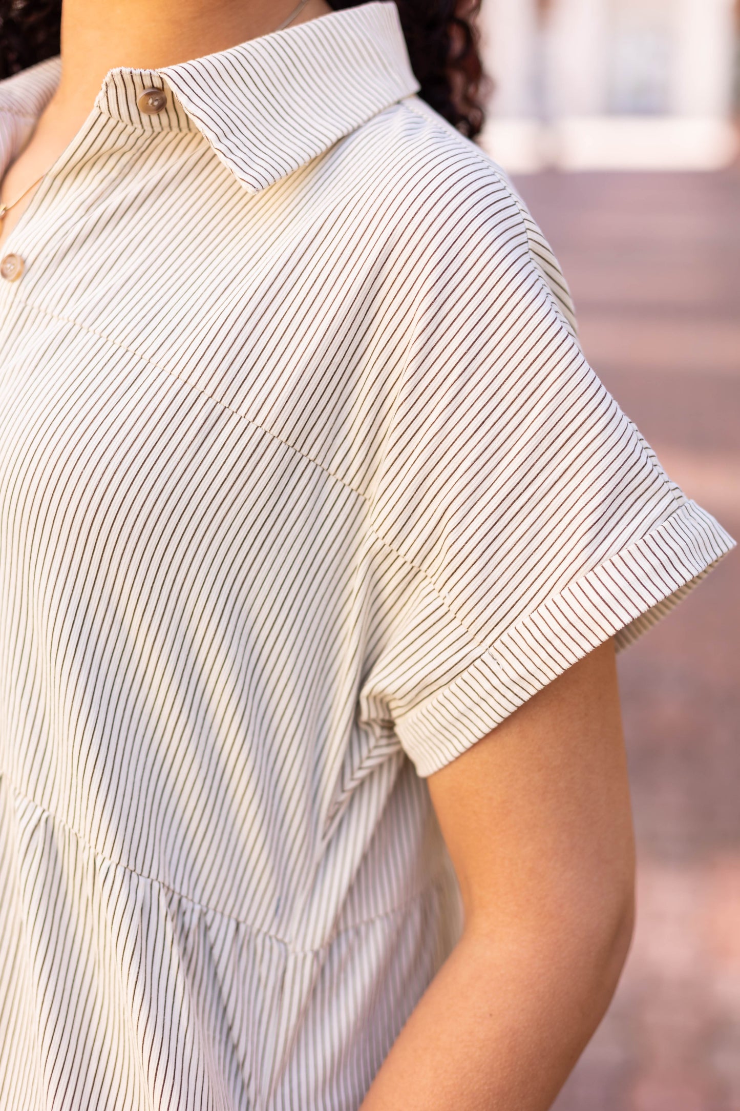Someone in a Carter Pin-Striped Midi Dress by Dogwood Cloth, made of 100% cotton, featuring short sleeves and a white fabric with thin black stripes. The dress highlights the torso and features exquisite corduroy texture detailing.
