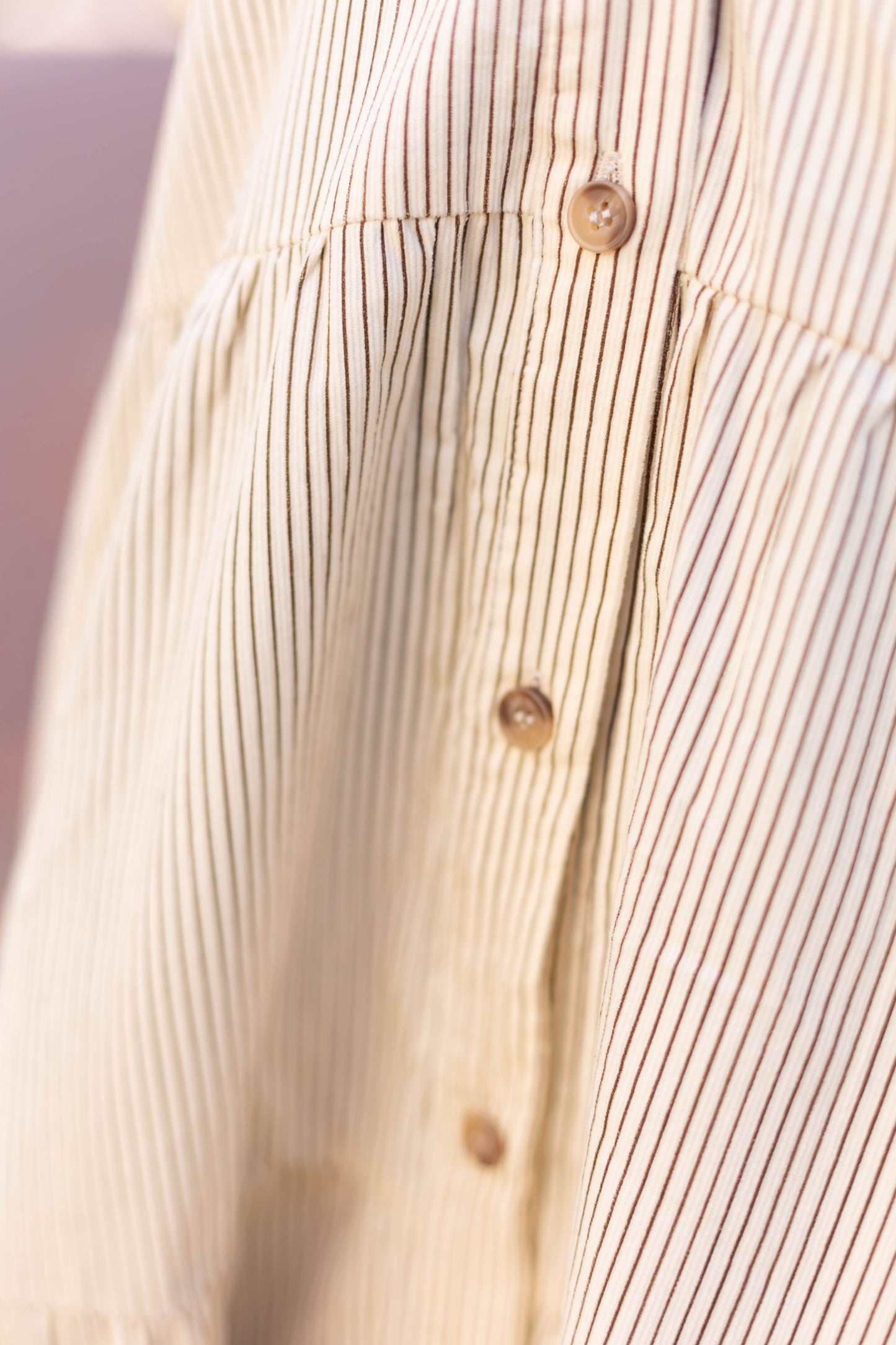 Close-up of the Carter Pin-Striped Midi Dress by Dogwood Cloth, featuring a beige and brown stripe pattern with vertical buttons, made from 100% cotton.