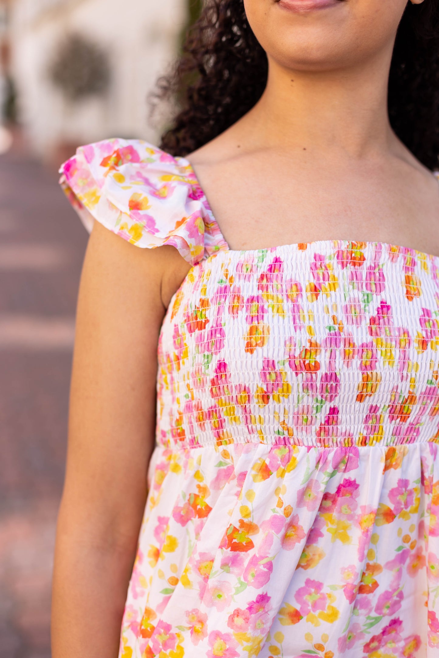 A person wearing the Stella Floral Midi by Dogwood Cloth, featuring a floral design and ruffled straps for a feminine touch, stands outdoors on a brick path.