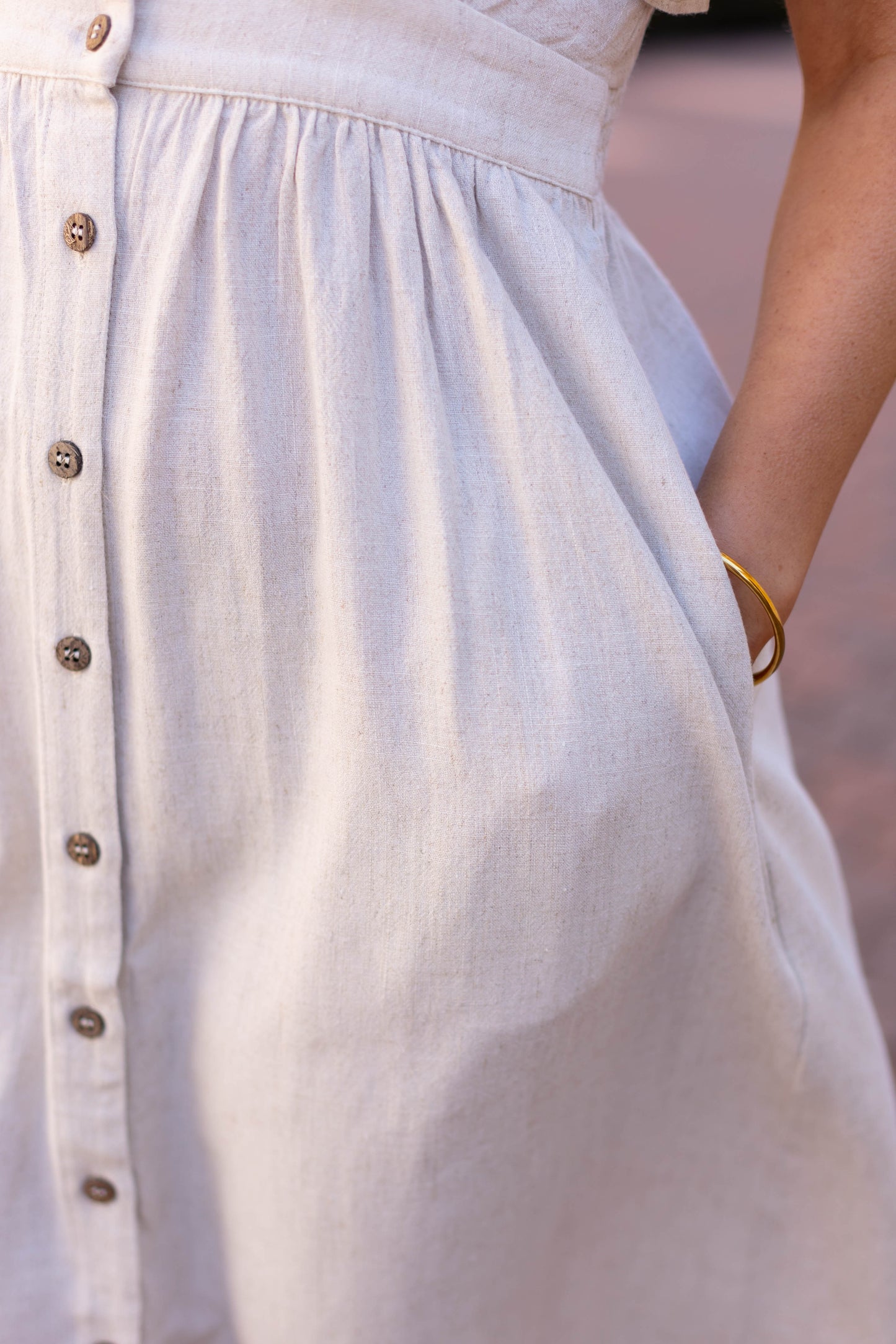 Close-up of the Dogwood Cloth Chelsea Linen Midi, an A-line summer dress in a light shade. A person’s right hand is in their pocket, adorned with a delicate gold bracelet.