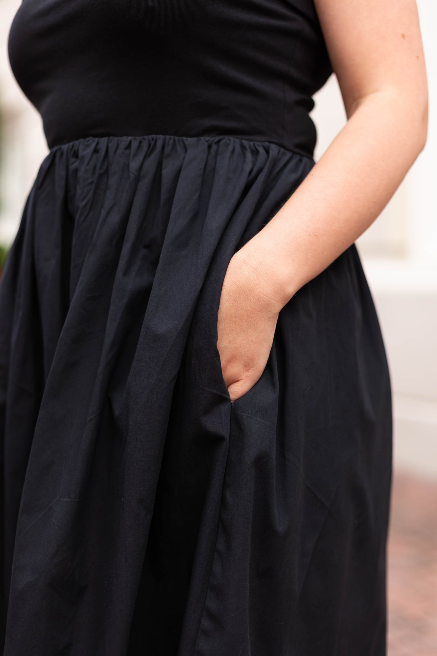 Wearing Dogwood Cloth’s The Evelyn Classic Midi, a person poses with one hand in a pocket, highlighting the skirt’s gathered fabric and the dress’s elegant A-line silhouette.