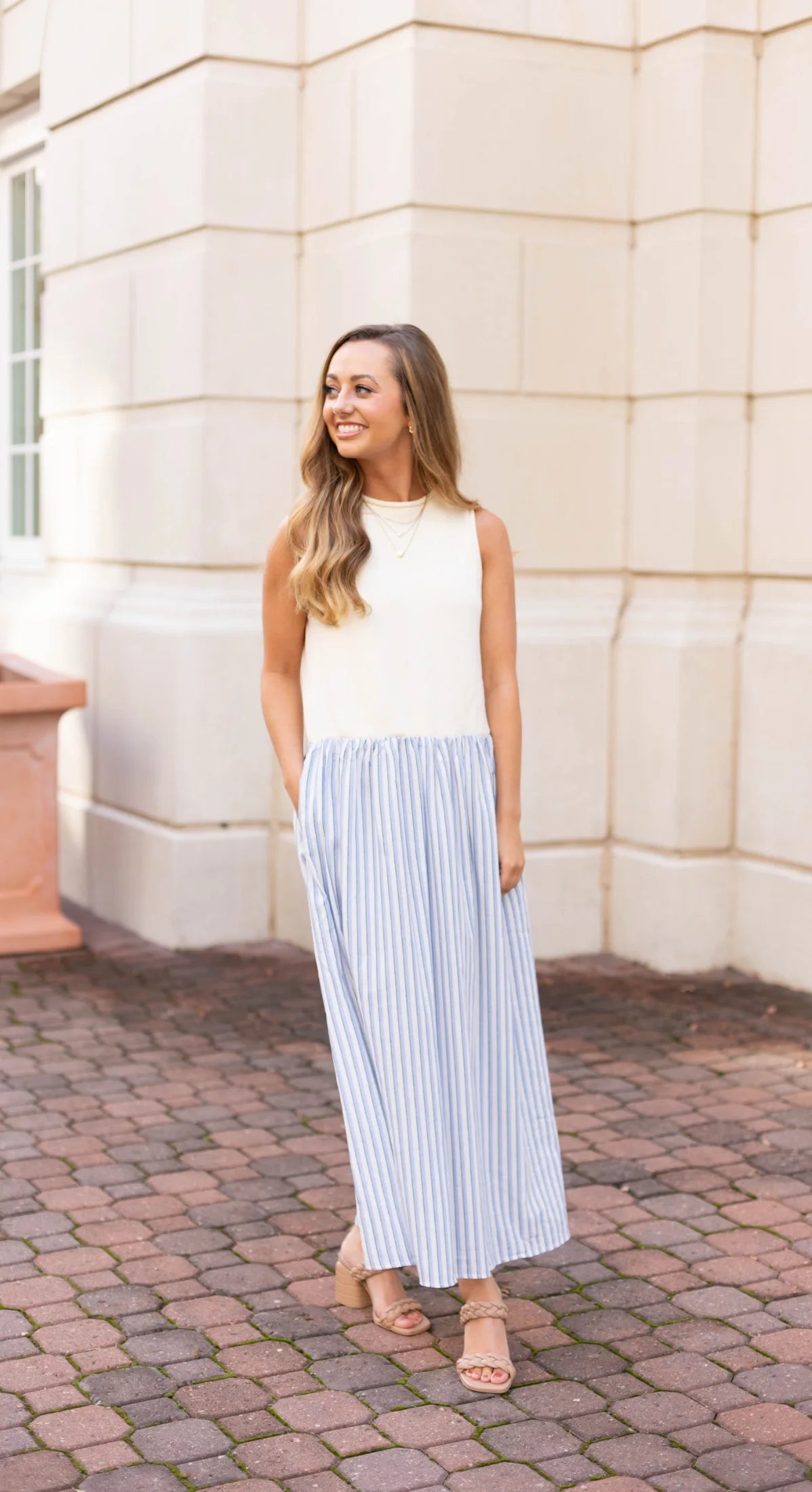 A woman wearing the Dogwood Cloth's Mia Contrast Midi stands outdoors on a brick path, smiling radiantly.