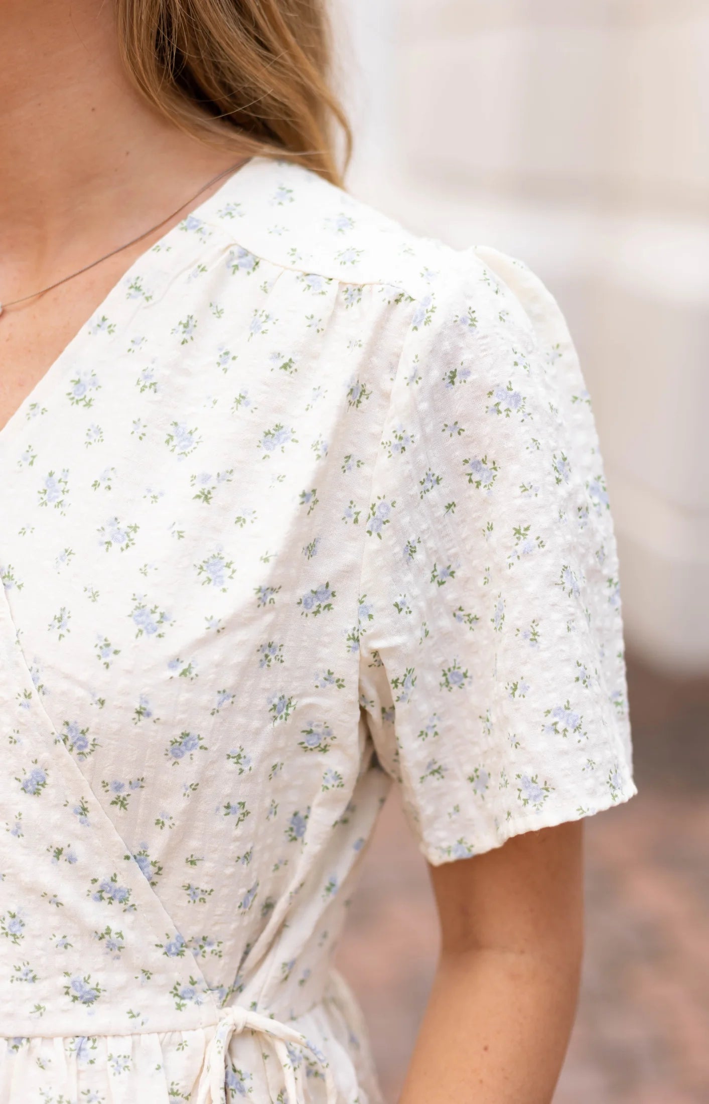 Close-up of a person wearing a vibrant floral pattern blouse with short sleeves outdoors, reminiscent of the Grace Wrap Dress by Dogwood Cloth.