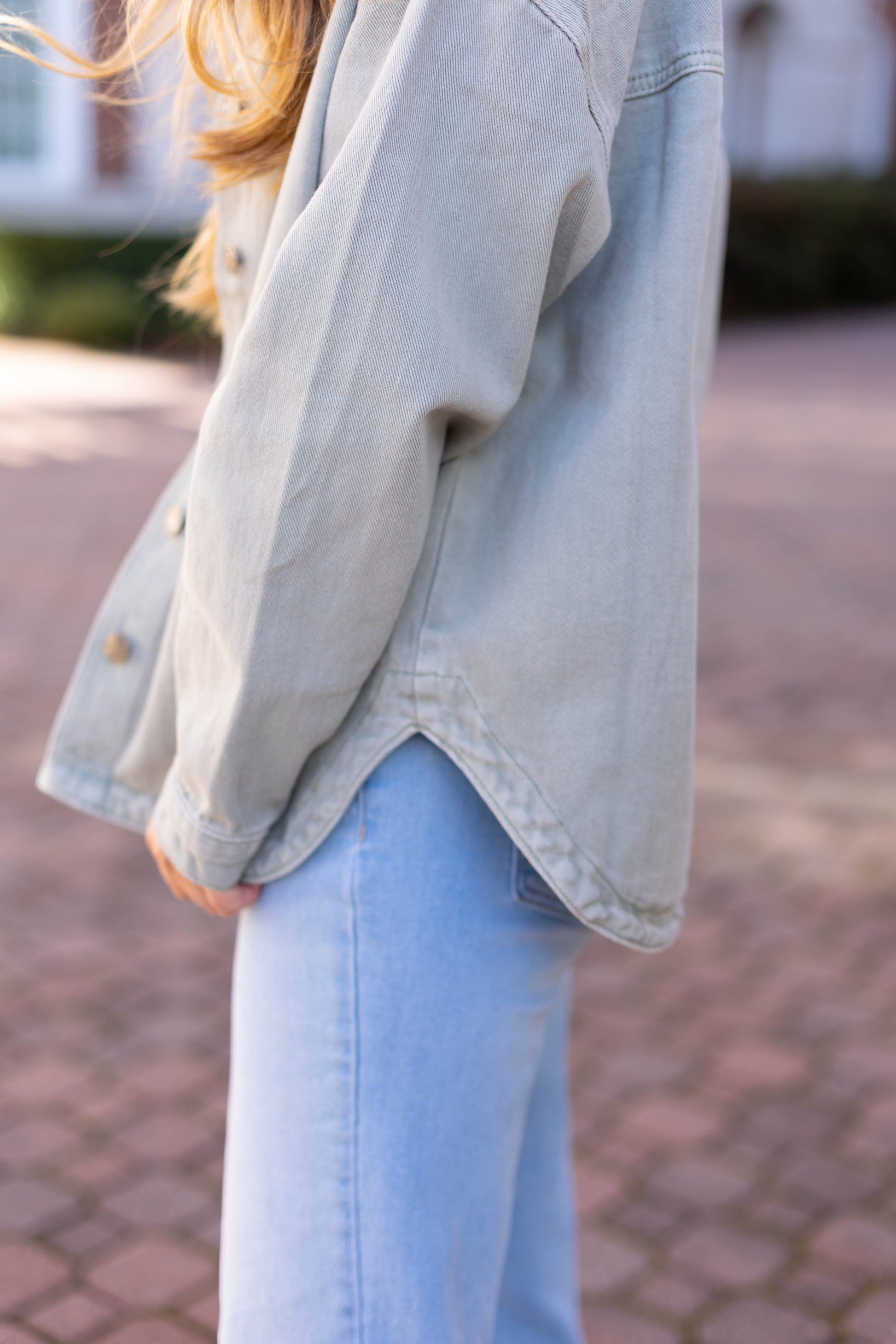 A person outdoors on a paved surface showcases elevated style with the Leah Denim Jacket by Dogwood Cloth, paired with jeans for this wardrobe essential look.