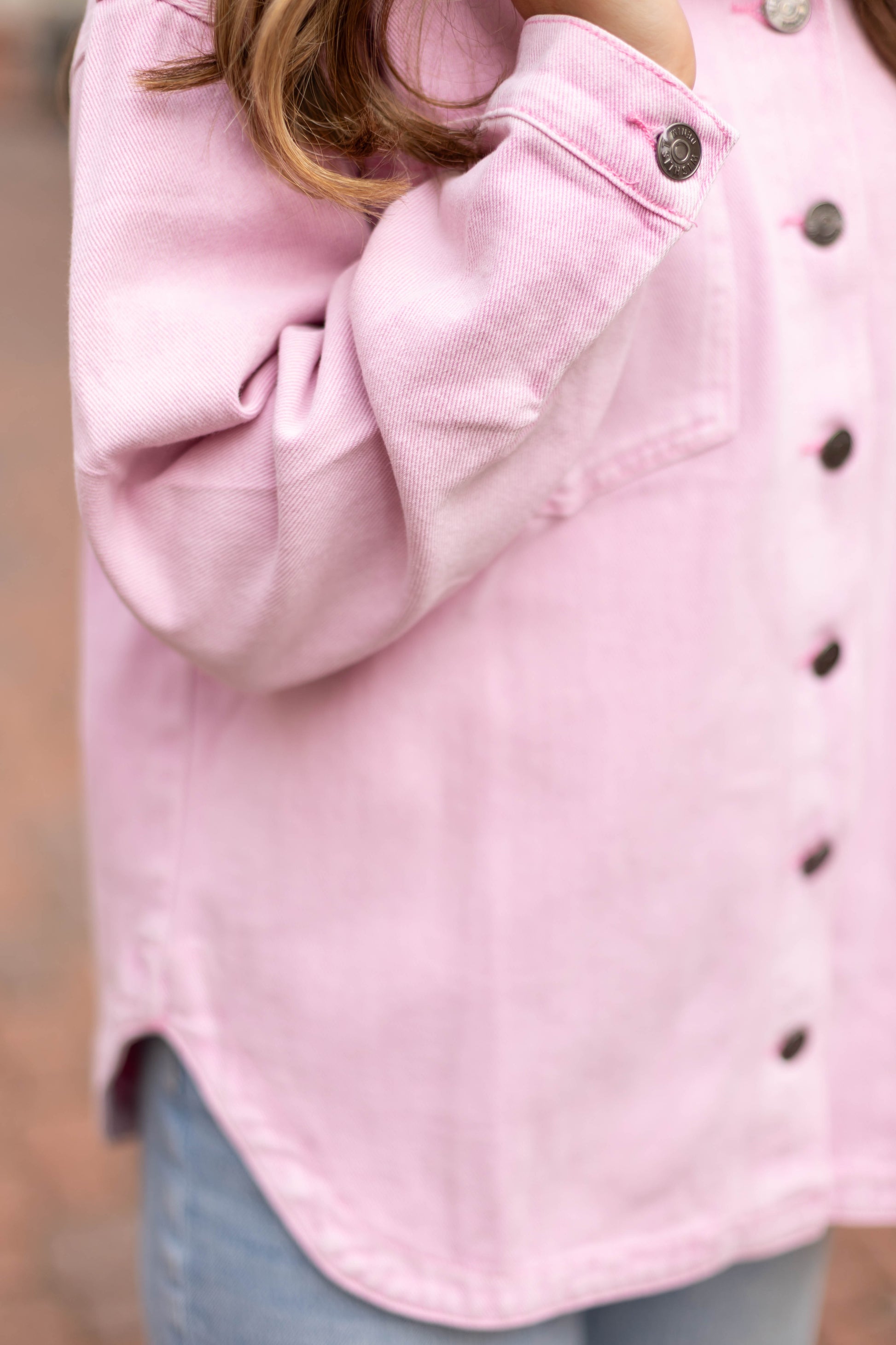 A person wears the Dogwood Cloth Leah Denim Jacket over a light pink button-up and light blue jeans, with long brown hair visible, standing outdoors.