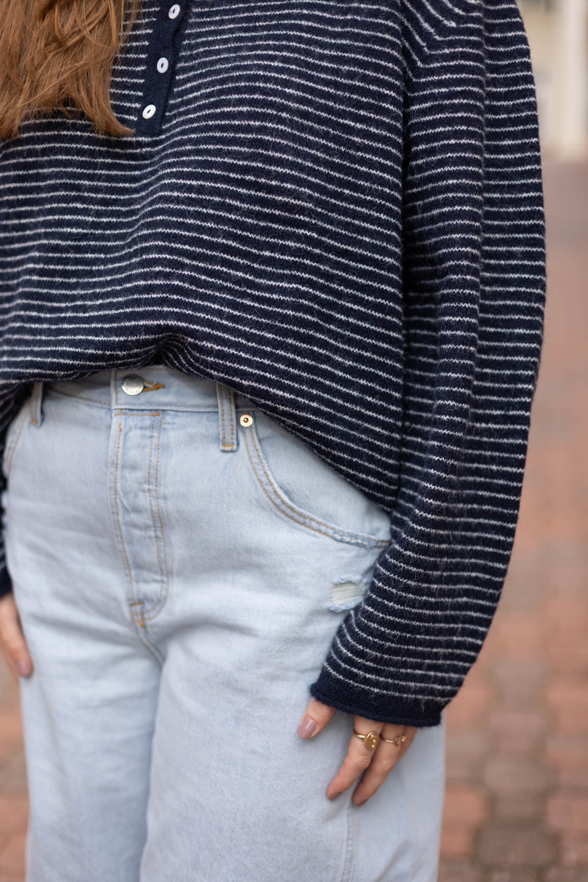 Wearing the Dogwood Cloth Anna Collared Henley striped knit top in navy and white, tucked into high-waisted light blue jeans, a person stands with hands resting at their sides.