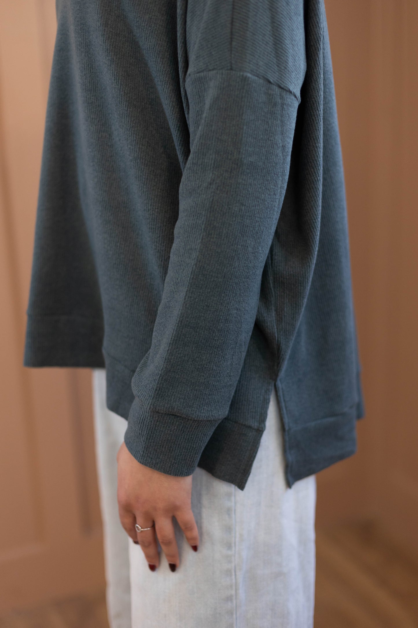 A person stands indoors, shown from the side with a relaxed arm and visible hand, wearing the Chandler Sage Top by Dogwood Cloth and light pants.