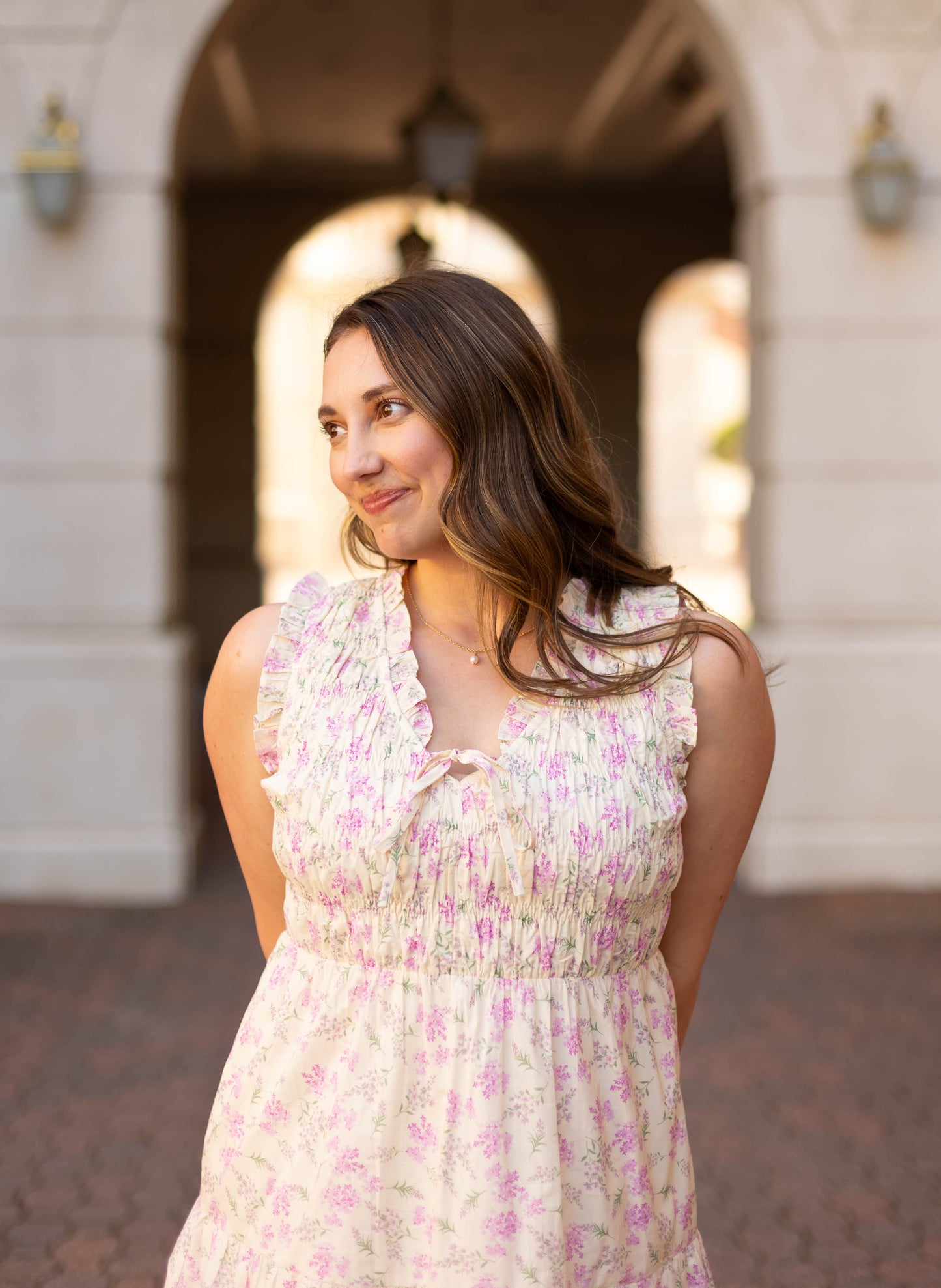 A woman with long brown hair wears the Sophia Floral Midi by Dogwood Cloth, standing outdoors and smiling as she looks to the side.